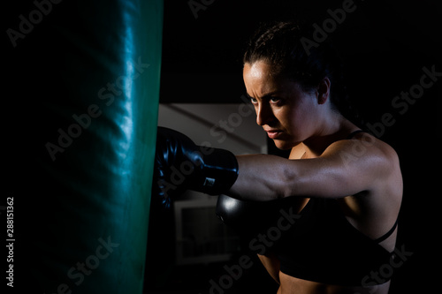 Young female boxer punching a bag on a sports training in a gym. © romul014
