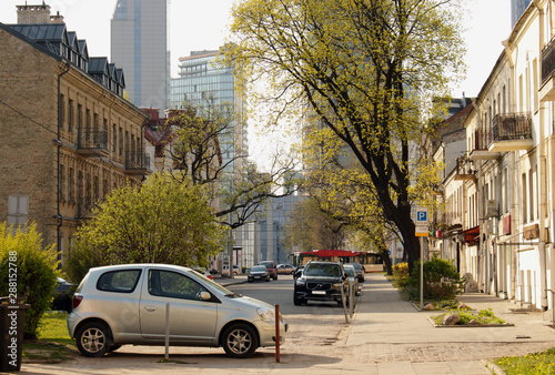 Street view of European city center with parked cars and greenery