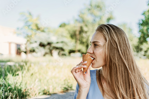 Summer city lifestyle girl portrait. Stylish young woman with ice cream in a waffle cone in her hand on a sunny summer hot day