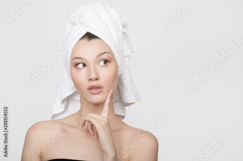 young woman with a towel on her head looks up. A hand near her face. Skin and body care concept
