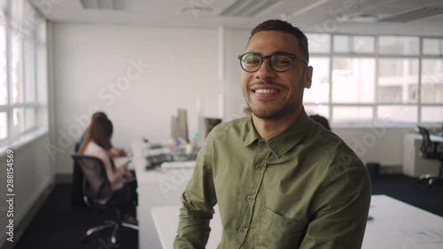Wallpaper Mural Portrait of successful professional young african american businessman smiling and looking at camera sitting in front of colleague working at background Torontodigital.ca