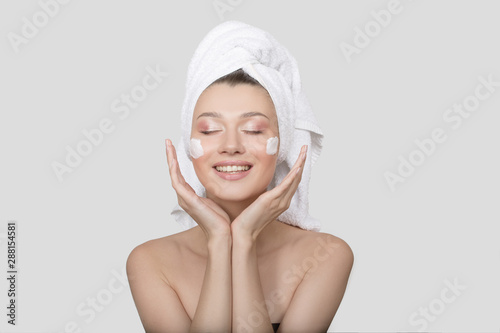 woman is laughing with cream on her face and a towel on her head. White background. Skin care concept