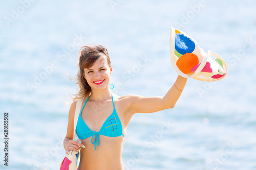 Beautiful girl affably waving her hat. A young woman waves her friends up in a swimsuit on the sea beach. photo