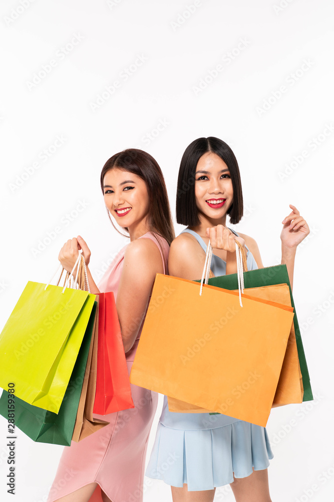 Two happy women holding packages on shoulders and looking at the camera over white background Two happy women holding packages on shoulders and looking at the camera over white background