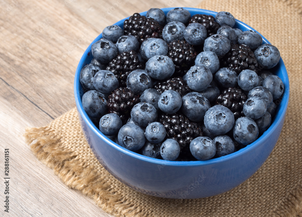 Bowl full of fresh blackberries and blueberries on a wooden background. Bowl full of fresh blackberries and blueberries on a wooden background.