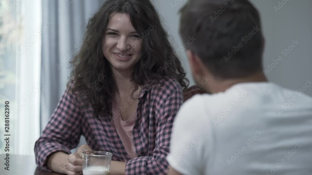 Portrait of happy woman drinking coffee while talking with her husband at home in the morning. Happy family resting at home. Friendly relationship. Shooting over the shoulder Portrait of happy woman drinking coffee while talking with her husband at home in the morning. Happy family resting at home. Friendly relationship. Shooting over the shoulder