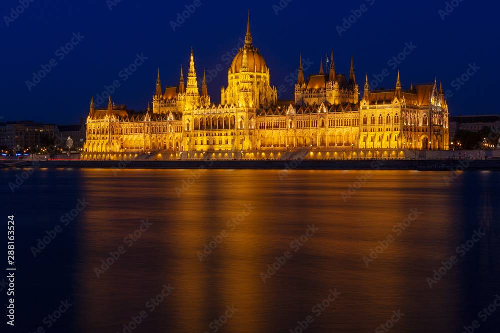 The Hungarian Parliament Building, a notable landmark of Hungary in Budapest. View of the main facade illuminated above the Danube river. Long exposure at a blue hour after sunset.