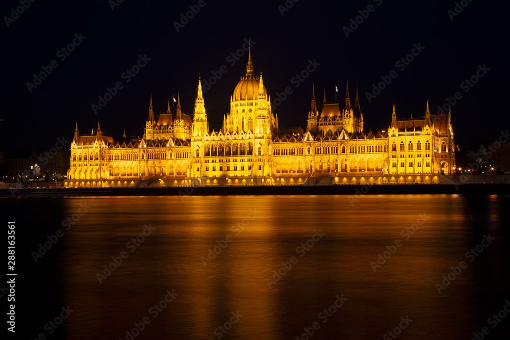 Fototapeta premium The Hungarian Parliament Building, a notable landmark of Hungary in Budapest. View of the main facade illuminated above the Danube river. Long exposure at a night.