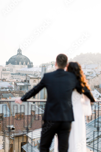 Back view of stylish beautiful couple Asians newlyweds standing on the terrace and watching on the panoramic city on a sunny day of their wedding
