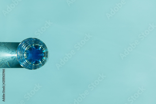 Glass of water with reflecting shadows on blue background. Healthy food concept. Top view. Copy space