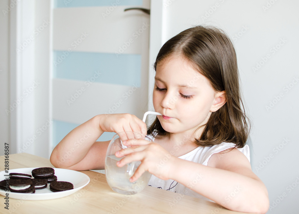 4 years old girl eating chocolate chip cookies and drinking milk at a table on a white wall background 4 years old girl eating chocolate chip cookies and drinking milk at a table on a white wall background