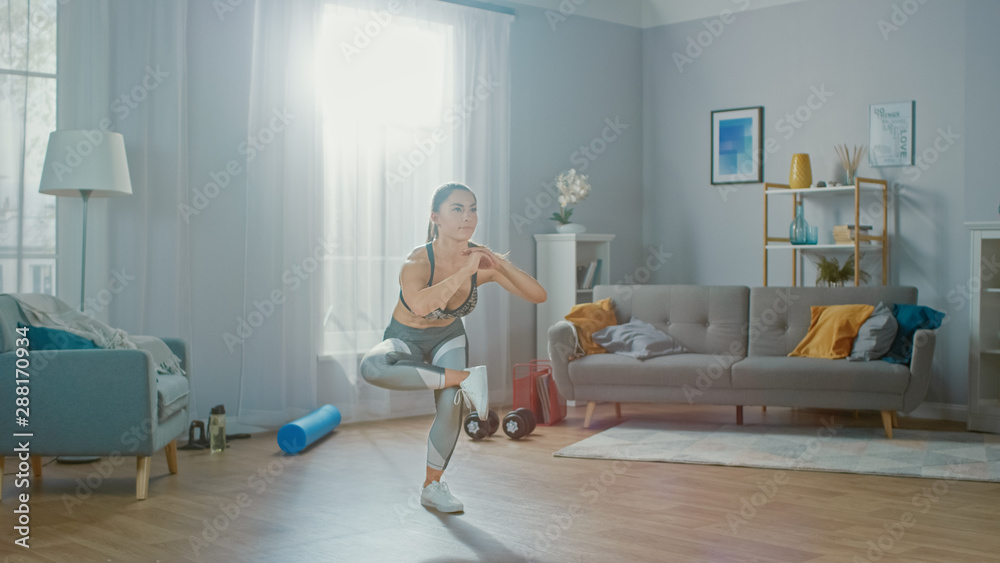 Beautiful Strong Fitness Girl in an Athletic Top is Doing Balance Yoga Exercises in Her Bright and Spacious Living Room with Minimalistic Interior.