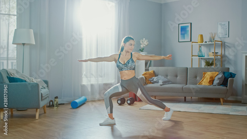 Beautiful Confident Fitness Girl in an Athletic Top is Doing Stretching Yoga Exercises in Her Bright and Spacious Living Room with Minimalistic Interior.