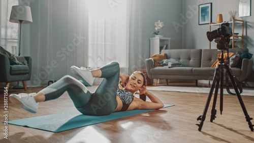 Beautiful Athletic Female Fitness Blogger is Talking on Camera and Recording her Crisscross Crunch Workout Routine in a Spacious and Bright Living Room with Cozy Modern Interior.