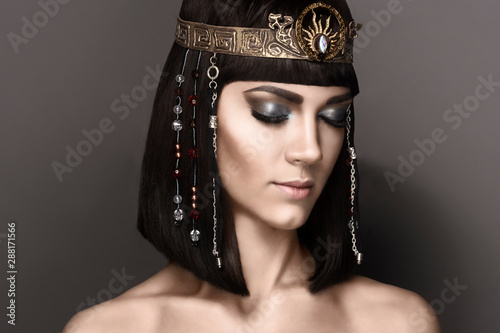 Glamorous closeup portrait of beautiful sexy stylish brunette young woman with bright makeup with perfect clean skin with gold jewelery. High fashion look. Beautiful Girl's Face Hairstyle Cleopatra