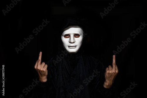 unrecognizable young man white mask and hoodie showing Middle Finger at Camera isolated on black Background.