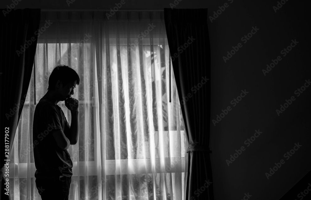 Fototapeta premium Alone man silhouette standing at the window closed with curtains in bedroom. Man stands at window alone, Depression and anxiety disorder concept.