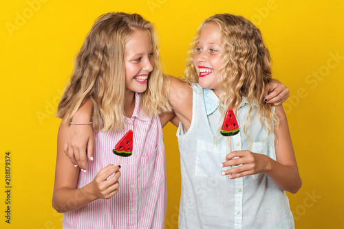 Happy smiling twins sisters hugging and laughing over yellow background. People, emotions, teens and friendship concept. Summer fashion, holidays, lifestyle
