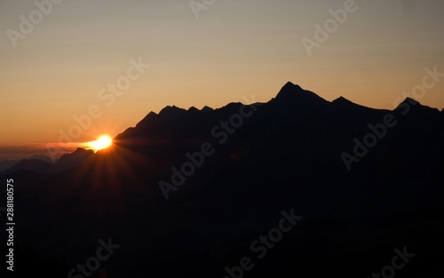 Beautiful sunrise in the swiss mountains, silhouette of mountain peaks backlit in the early morning.