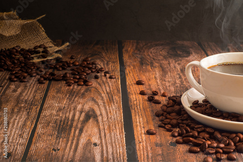 Hot coffee in a white coffee mug is placed on a wooden table. With coffee beans in the sack And placed in groups near the coffee cup
