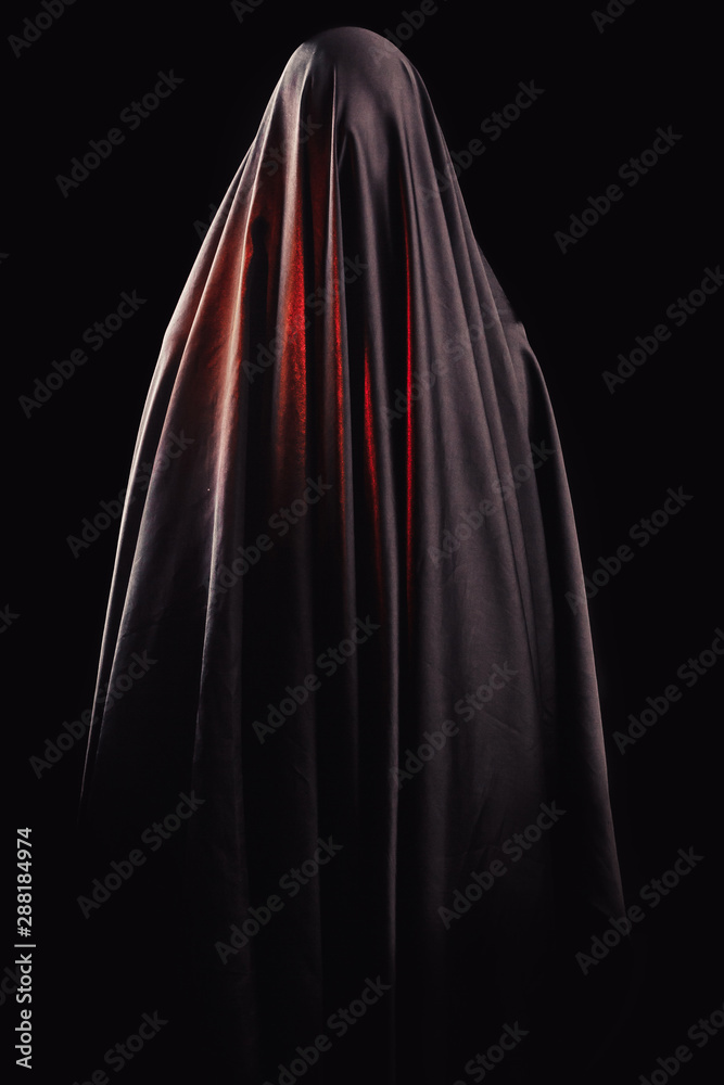 woman covered with black cloth stands on an isolated black background. faceless death concept woman covered with black cloth stands on an isolated black background. faceless death concept