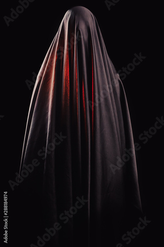 woman covered with black cloth stands on an isolated black background. faceless death concept