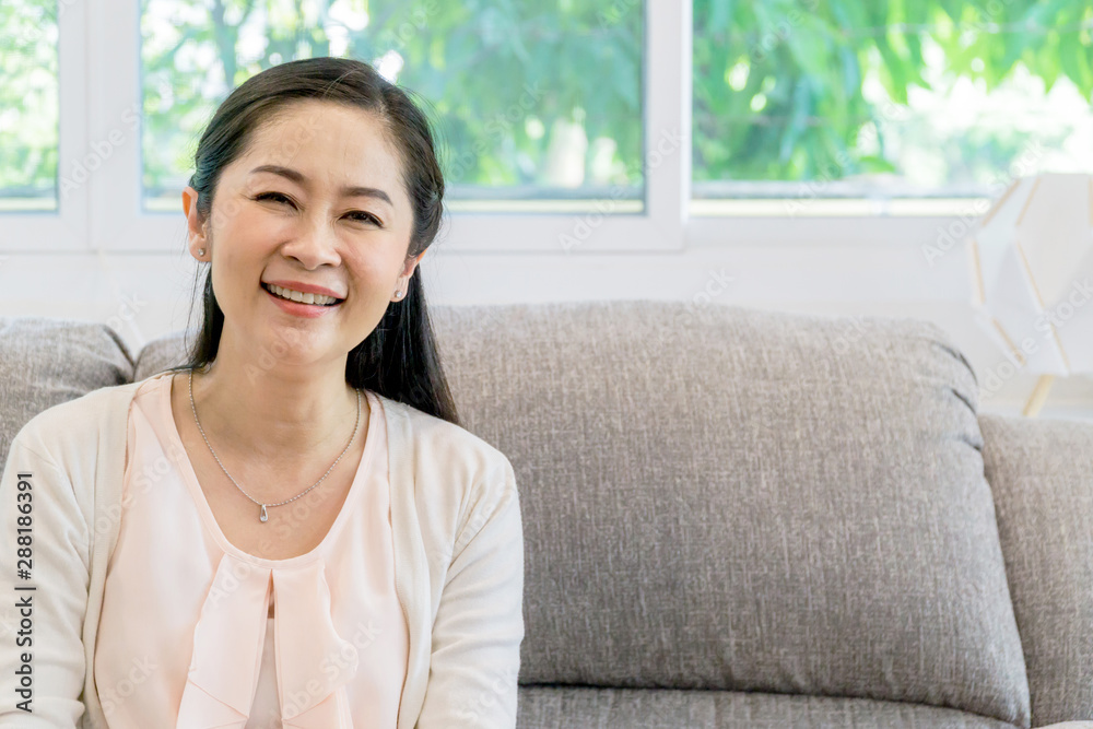 Middle aged Asian woman portrait sitting on a couch indoors. Middle aged Asian woman portrait sitting on a couch indoors.
