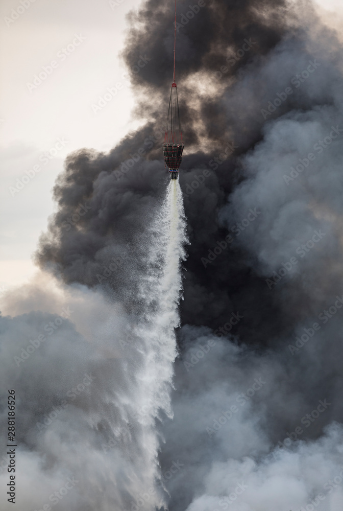 helicopter extinguishes a fire from a basket of water