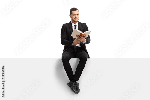 Businessman sitting on a banner with a book and looking at the camera © Ljupco Smokovski