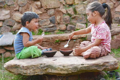 Little latin children sitting on the big stone and eating from rural bowl.