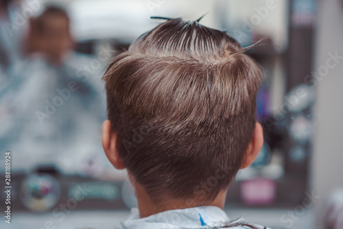 Boy getting haircut by barber in barbershop. © Artem