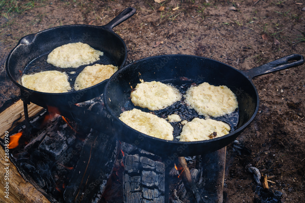 Cooking on a fire in the forest. on the grid are the pot and pan. in a frying pan fried pancakes Cooking on a fire in the forest. on the grid are the pot and pan. in a frying pan fried pancakes