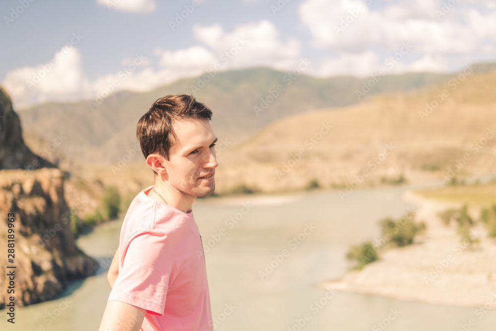young smiling man in a pink t-shirt on a background of mountains on a sunny summer day