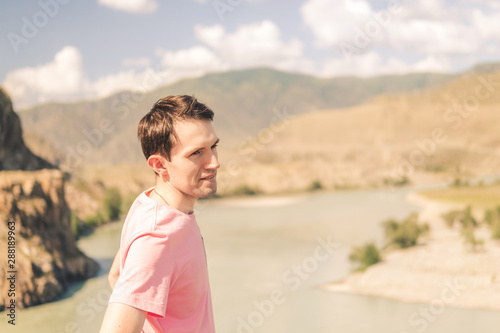 young smiling man in a pink t-shirt on a background of mountains on a sunny summer day © Андрей К