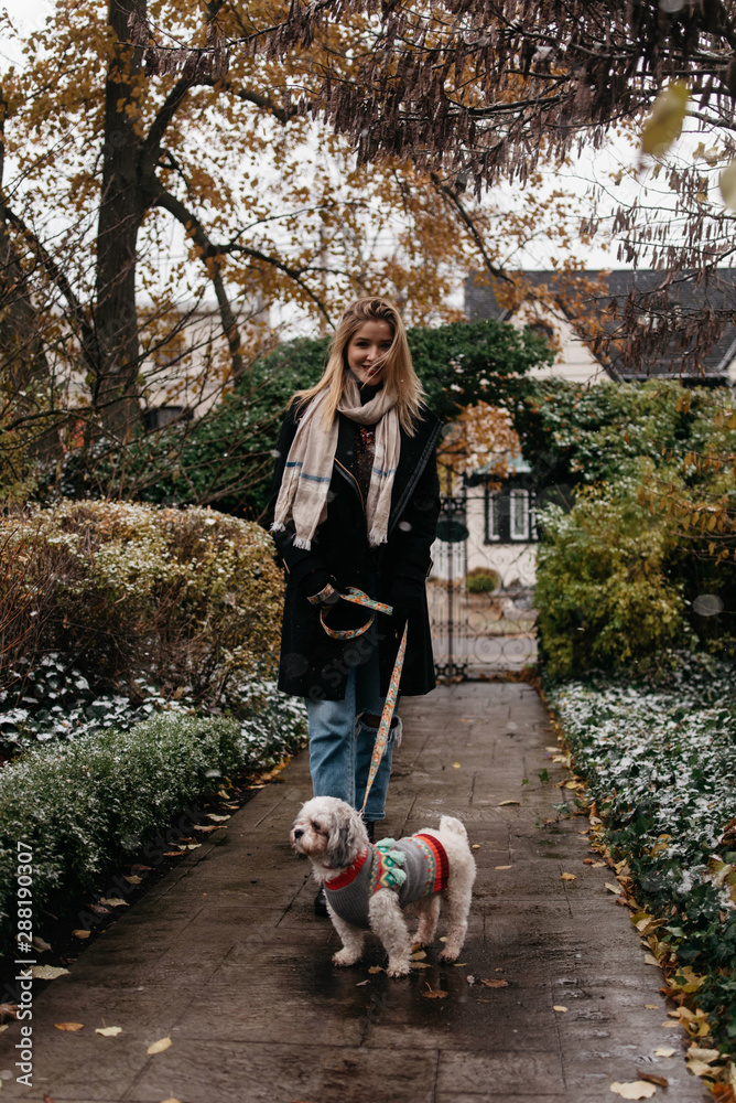 A woman in her twenties walking her small dog in the snow A woman in her twenties walking her small dog in the snow