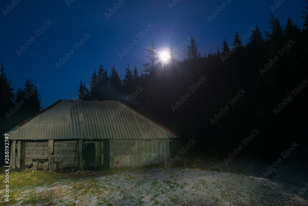 Old house in forest at night with moon light and stars on dark blue sky