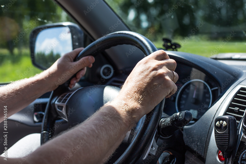 a man with two hands holds the steering wheel of a car and drives a car, outside the window a summer day