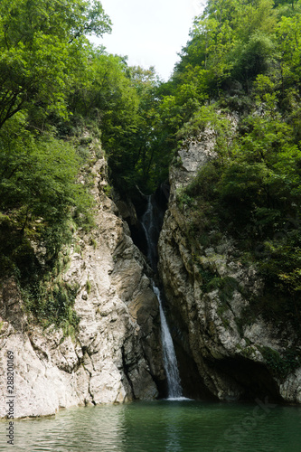 Waterfall in a crevice between the rocks behind the trees. Agur waterfalls in Sochi