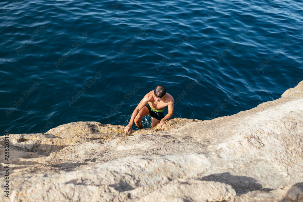 Man climbing rock going out from water Man climbing rock going out from water