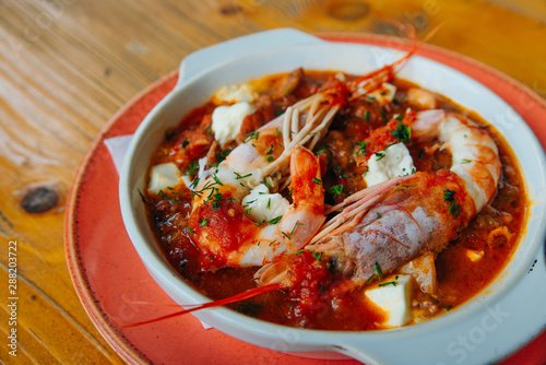 Greek traditional food. Oven backed prawns with feta, tomato, paprika, thyme in a traditional ceramic form on a abstract background. Healthy eating concept. Mediterranean lifestyle. photo