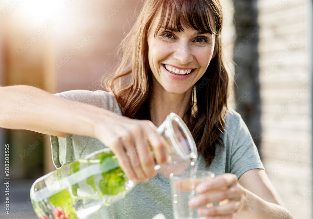 Portrait of happy woman pouring infused water into glass Portrait of happy woman pouring infused water into glass