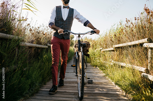 Well dressed man walking with his bike on a wooden walkway in the countryside after work photo