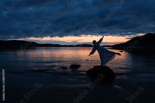 A girl stands on the shore of the Barents Sea at sunrise