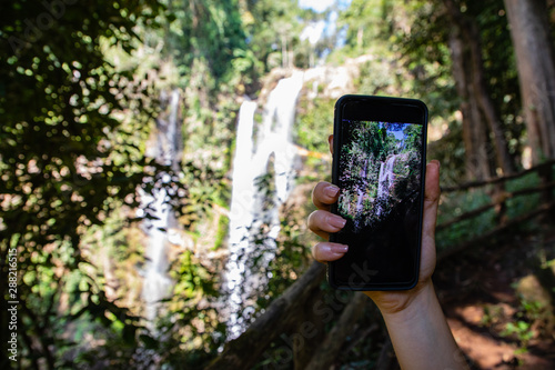 Woman hand holding a phone making a photograph of a waterfall