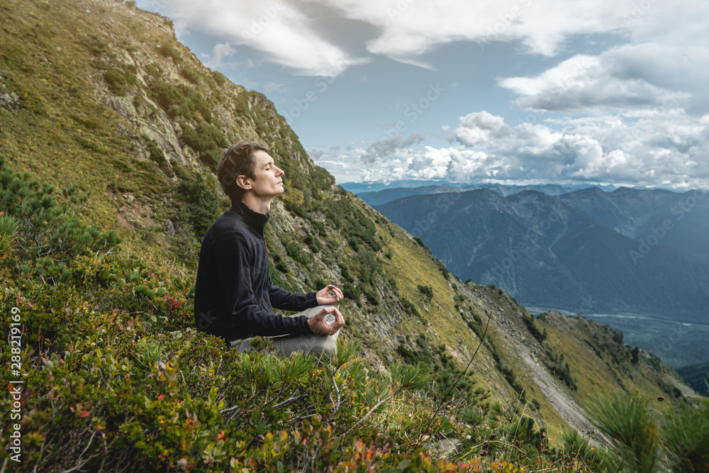 Man is sitting on a stone hillside, hands looking at the view from the heights and enjoys the freedom