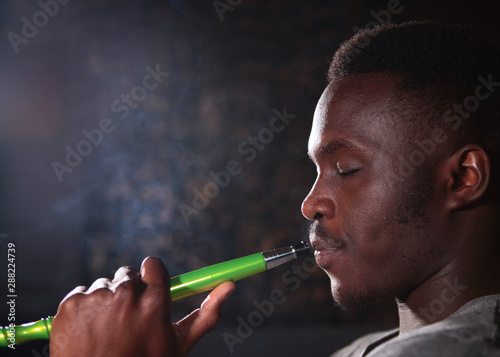 Portrait of an African American on a black background. A man smokes a hookah.