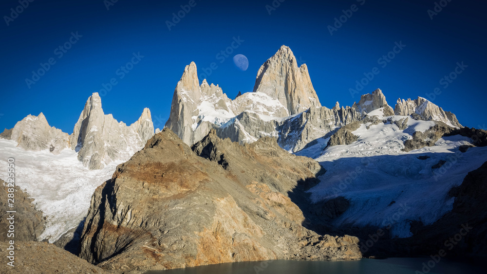Amazing morning shot at the base of Mount Fitz Roy (or Mount Chalten), the moon is huge in the middle of the sky. In the surface there is a lake called 