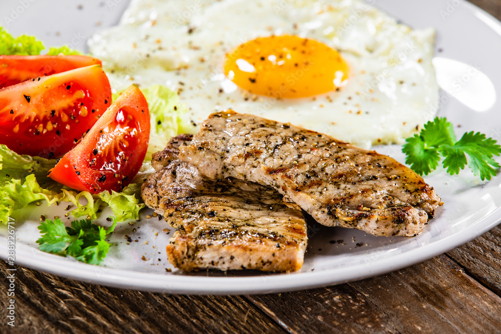 Grilled steaks with fried egg and vegetables on white plate Grilled steaks with fried egg and vegetables on white plate