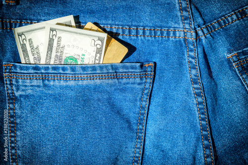 Visa plastic bank card with dollar cash in blue jeans pocket- money concept