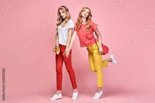 Two easy-going happy hipster Woman dance Fun in Stylish fashion colored coral yellow pants. Beautiful excited Girl in summer Trendy outfit, sneakers jump laughing. Creative dancing fashionable concept